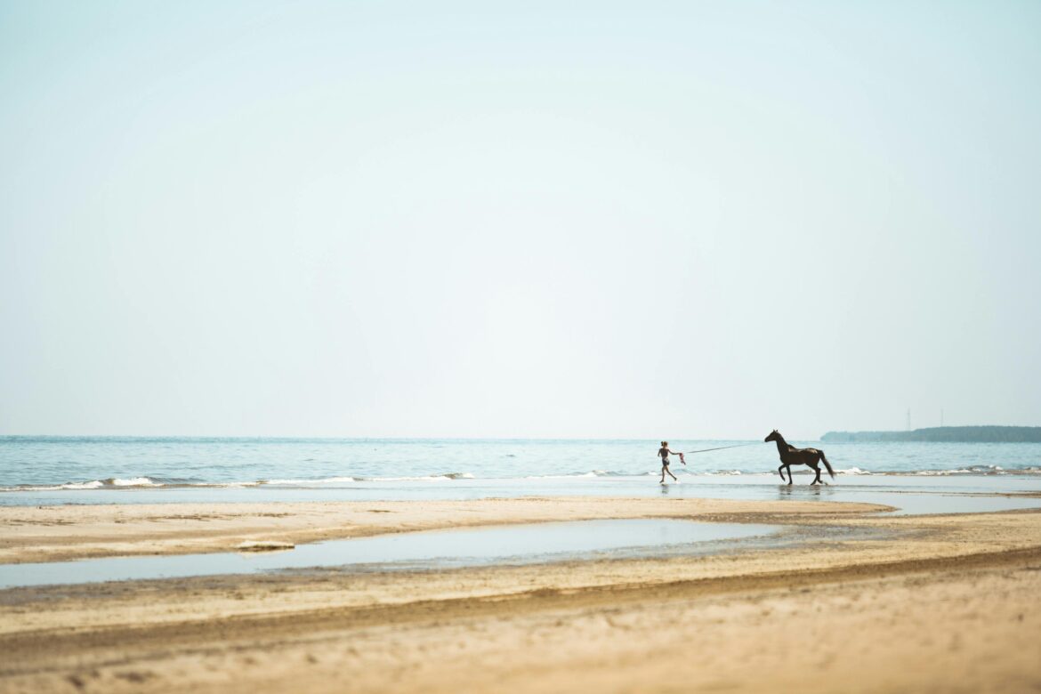 A person running with a horse along a quiet beach, one of the secret spots in Kurzeme perfect for peaceful moments by the sea.